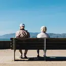 Home i dona grans asseguts en un banc d'esquenes mirant un paisatge de muntanya