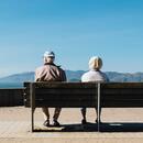 Home i dona grans asseguts en un banc d'esquenes mirant un paisatge de muntanya