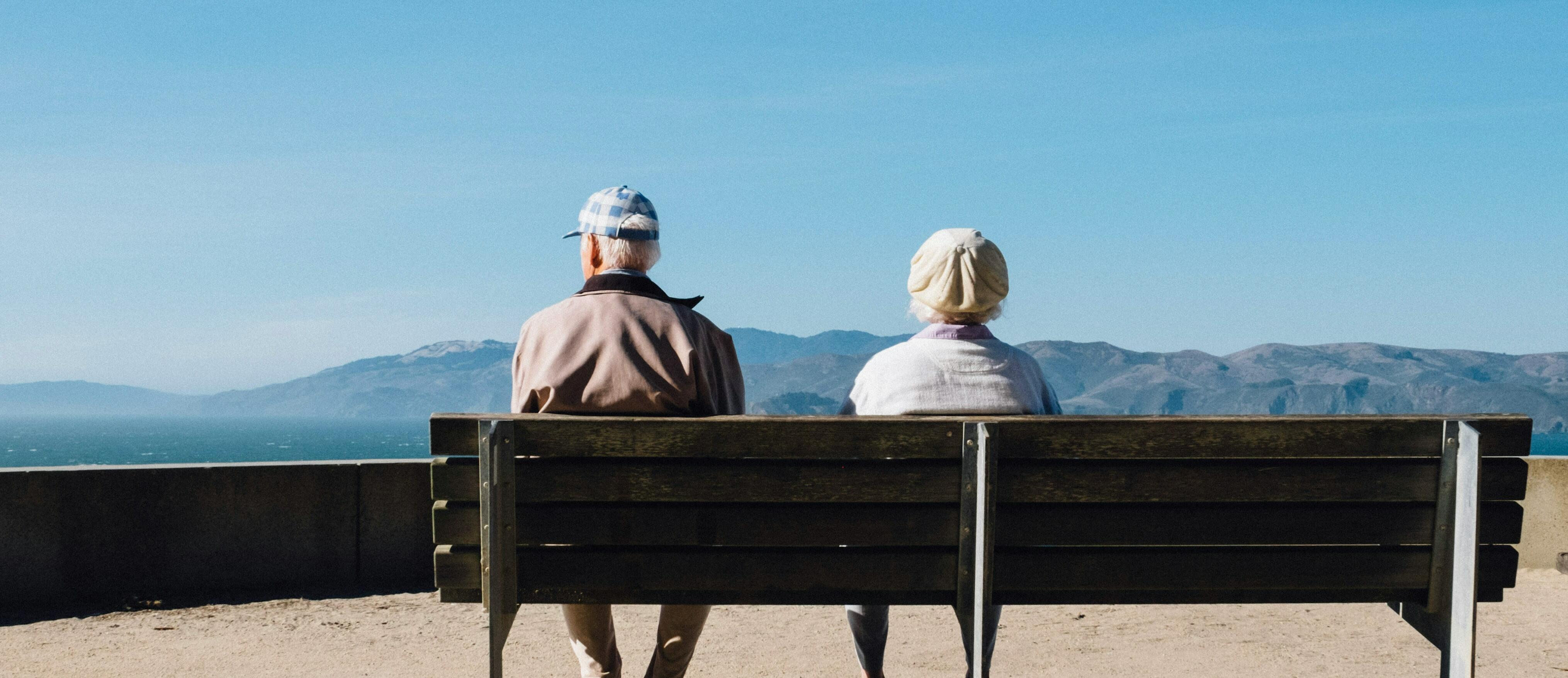 Home i dona grans asseguts en un banc d'esquenes mirant un paisatge de muntanya