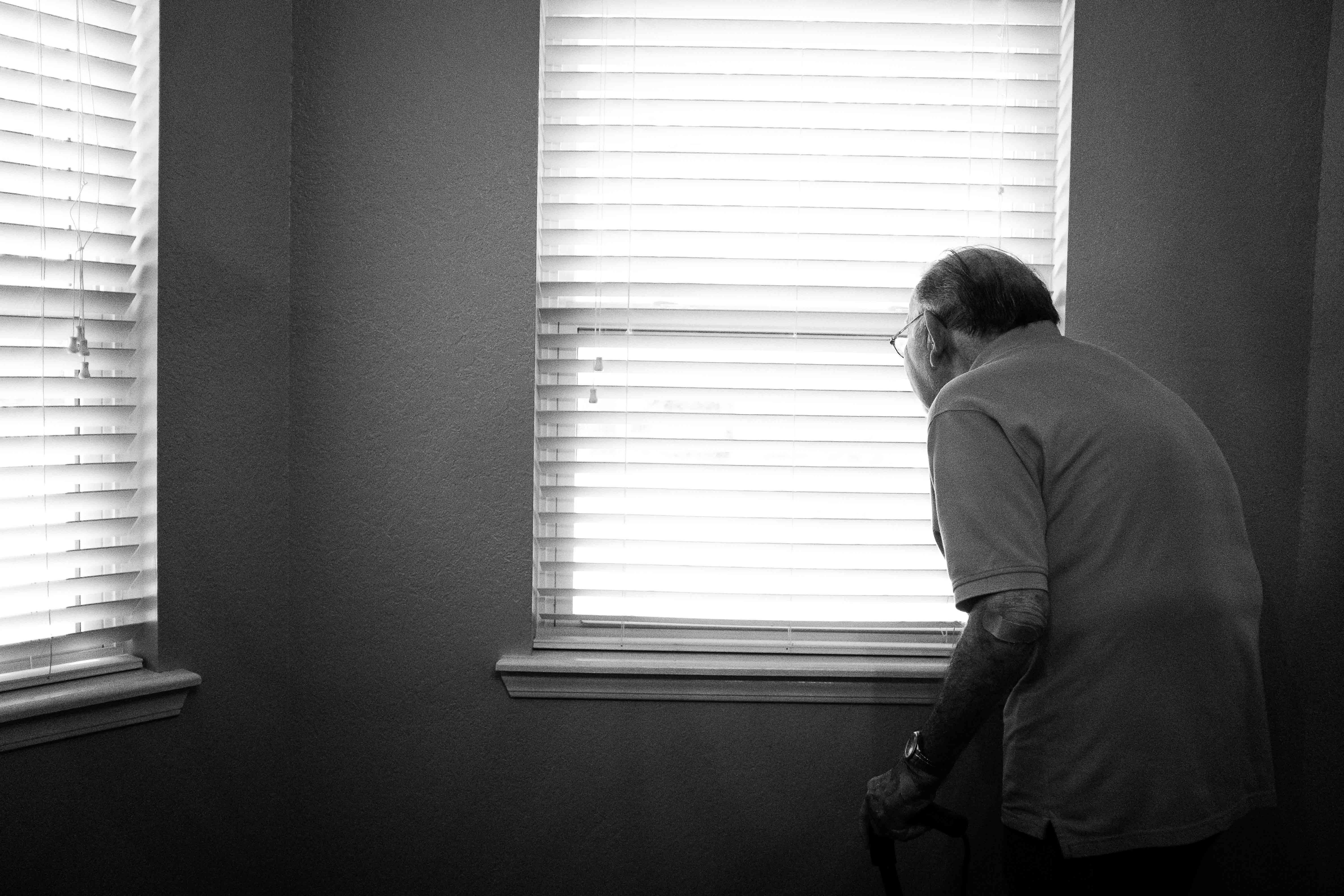 Una persona gran mirant a través de les escletxes de la persiana en una finestra.