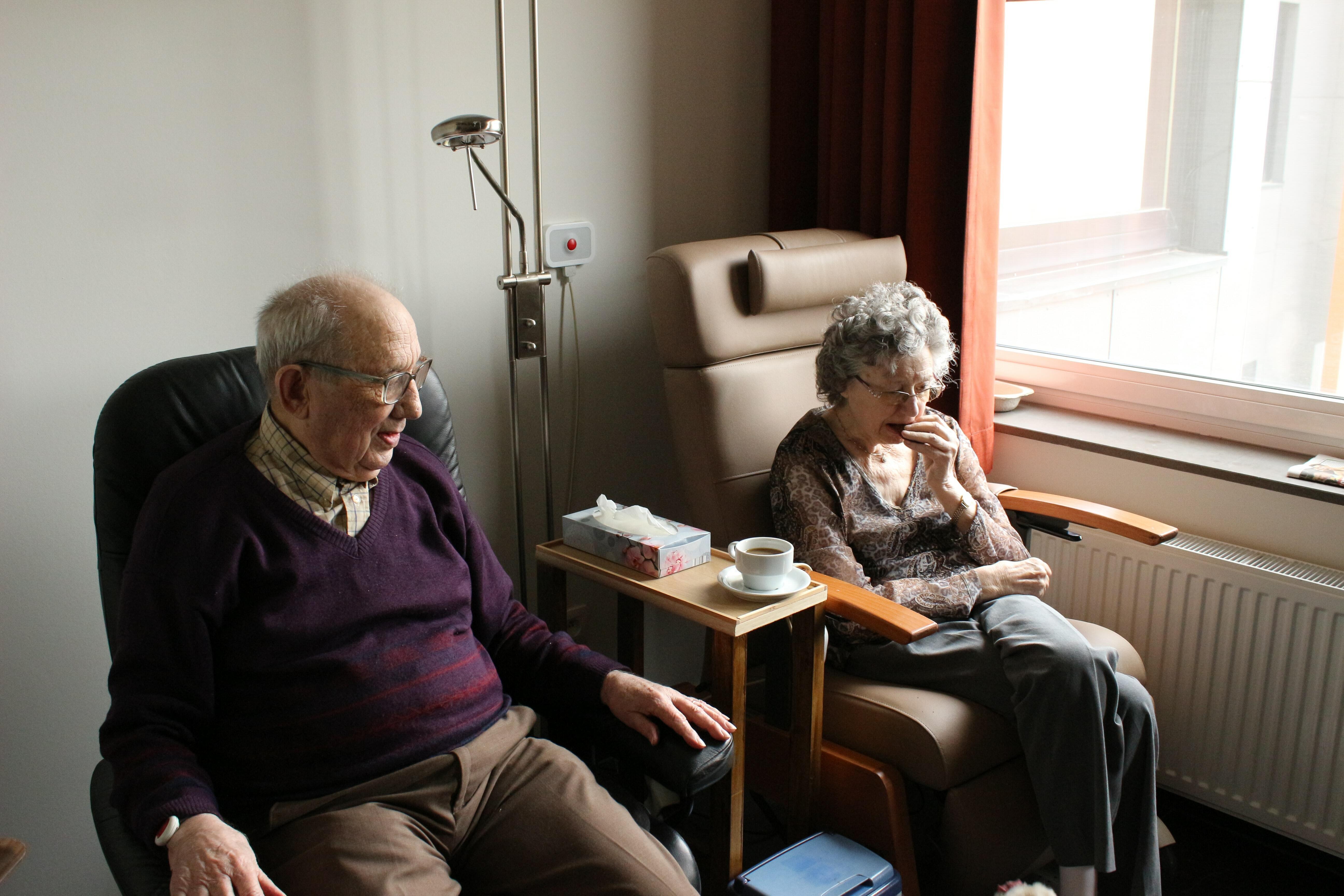 Una parella de persones d'edat avançada asseguts en una cambra d'un centre residencial.