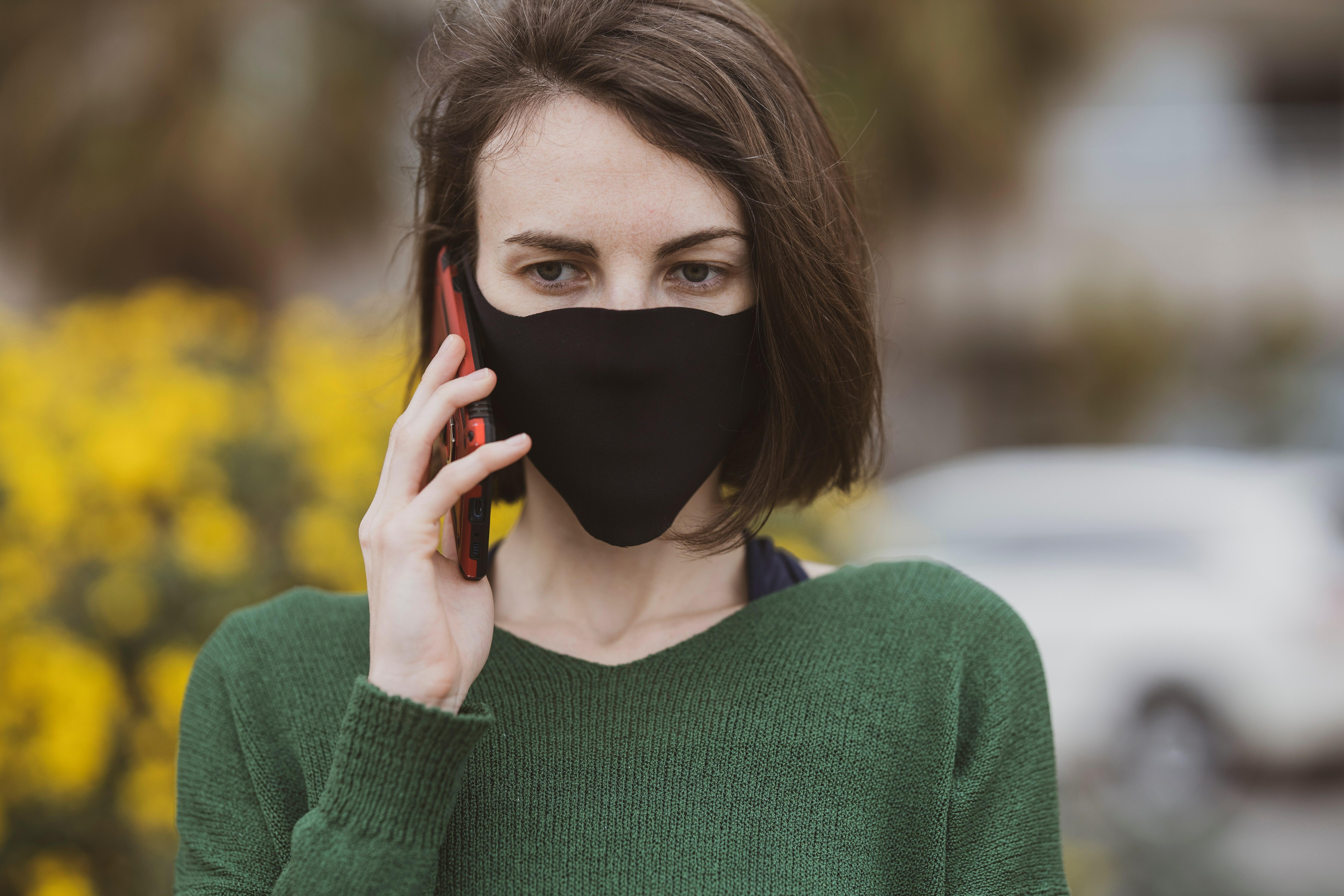Una jove amb mascareta negra a la cara parla per telèfon mòbil.