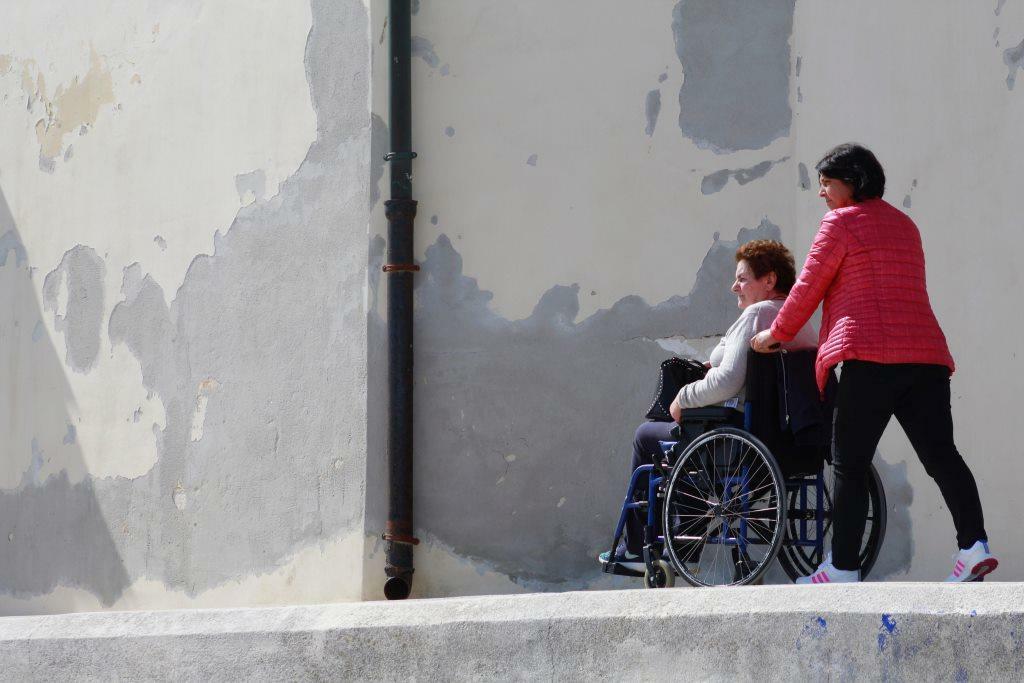 Una dona empenta una senyora en una cadira de rodes pel carrer.